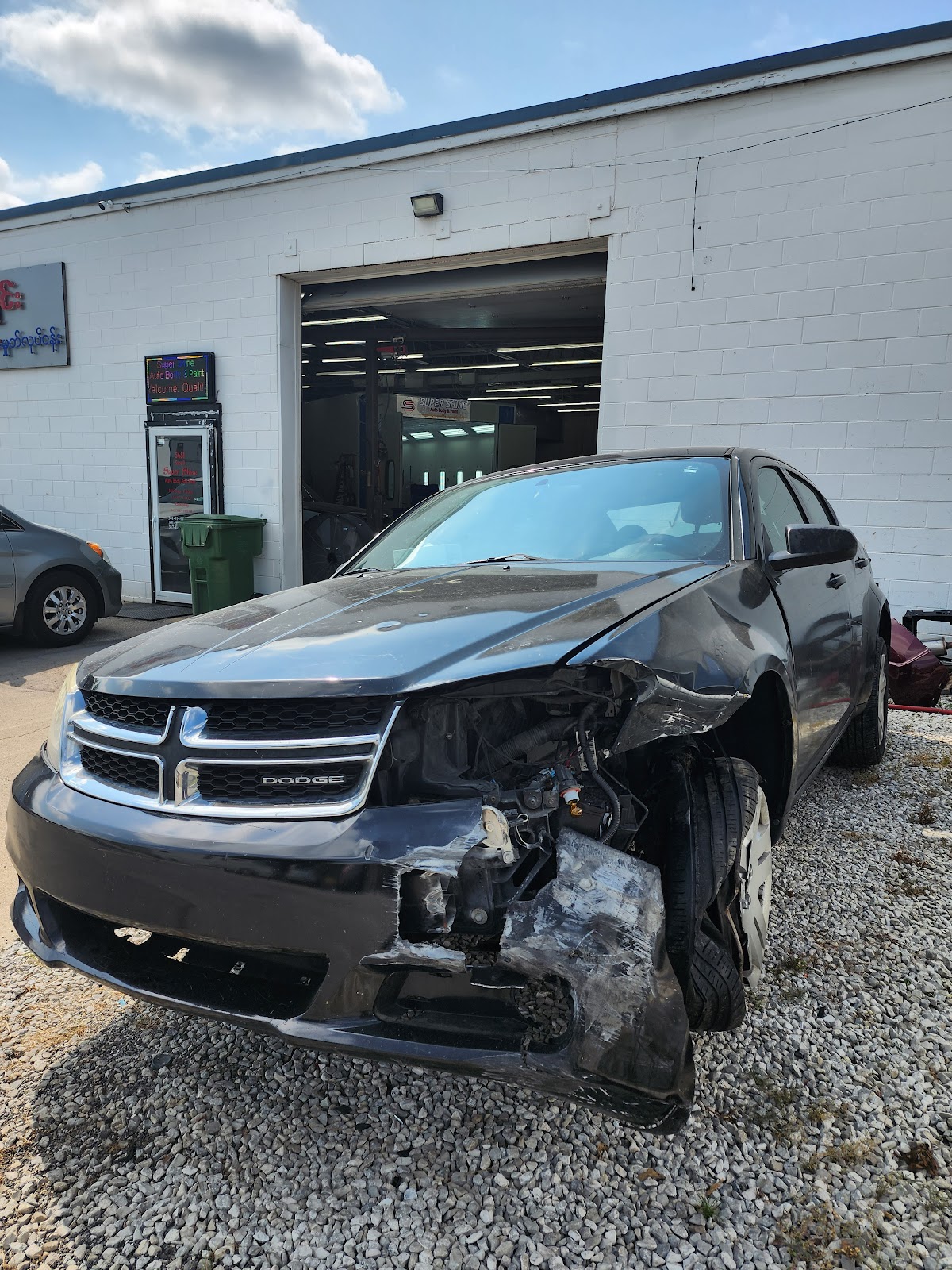 A car with significant front-end collision damage parked outside the Super Shine Auto Body shop